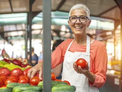 A woman stall owner holding a tomato at her stall with many vegetables